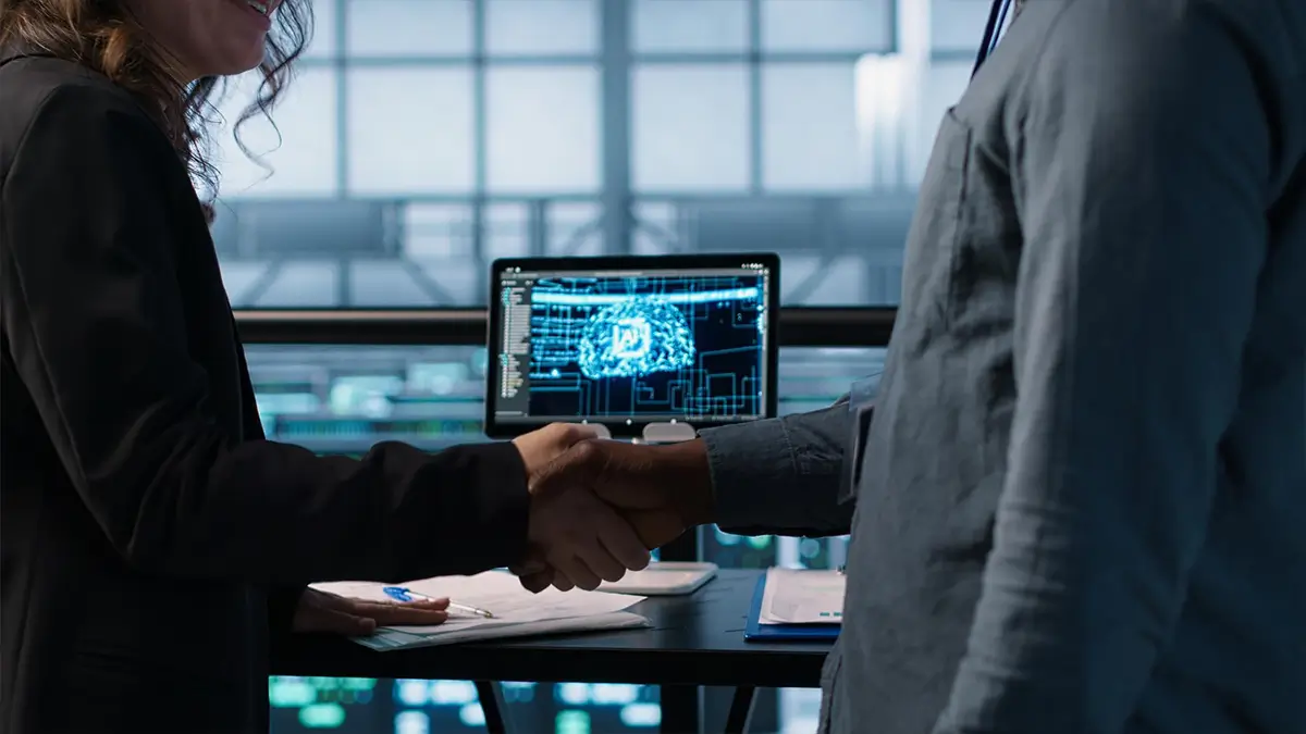 Aperto de mão profissional entre um homem e uma mulher em um escritório moderno, com um monitor ao fundo exibindo uma representação digital de um cérebro com o símbolo de 'AI' e como isso pode melhorar a Governança para instituições sem fins lucrativos.